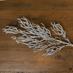 Flockpatch artificial branch lying diagonally on a wooden surface, with spreading brown offshoots covered in white snow-effect texture.