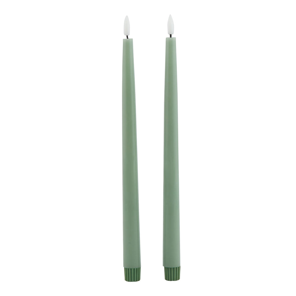 Two slim sage green LED dinner candles with pale flame-shaped inserts and darker ribbed base caps against white.