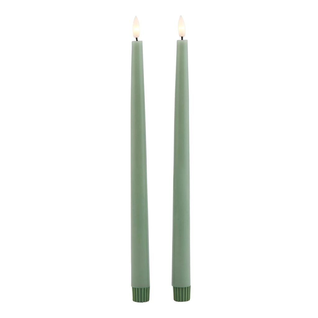 Full view of two green LED dinner candles with flame-shaped tips shown glowing pale yellow and ribbed dark green bases.