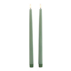 Full view of two green LED dinner candles with flame-shaped tips shown glowing pale yellow and ribbed dark green bases.
