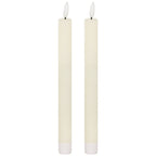 Two matching slender ivory dinner candles with white flame-shaped tips on dark posts and ribbed white lower sleeves, against a white background.