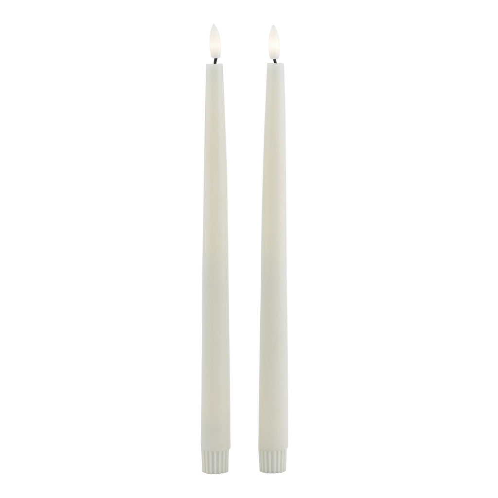 Full-length view of two pale LED dinner candles with fluted lower caps and flame-shaped inserts pictured with warm white centres.