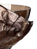 Detail of the bronze-toned metal folds and textured surface, with the curved glass bowl visible behind them.