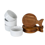 White bowls grouped beside stacked brown fish-shaped trays, with one bowl tilted and an upright tray showing its circular recess and forked tail.