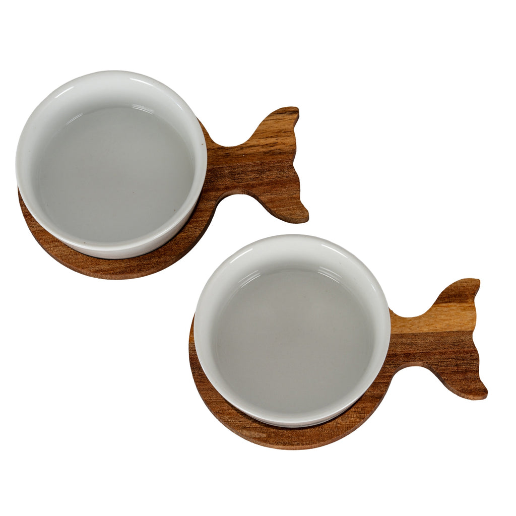 Overhead view of two round white bowls seated on brown fish-shaped bases, arranged diagonally with their tails to the right.