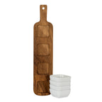 Serving board standing upright to show four rounded-square recesses and warm brown grain, beside a stack of four glossy white bowls.