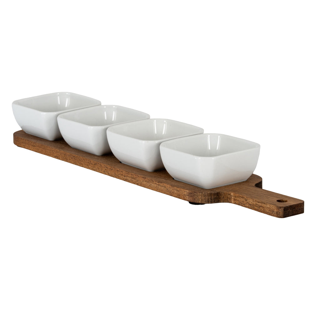 Angled view of four glossy white rounded-square bowls arranged on a warm brown paddle-shaped board, with its handle extending to the right.
