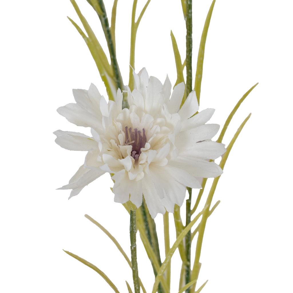 Close-up of a white artificial flowerhead showing overlapping textured petals and a muted purple centre, with green stems and slender leaves behind.