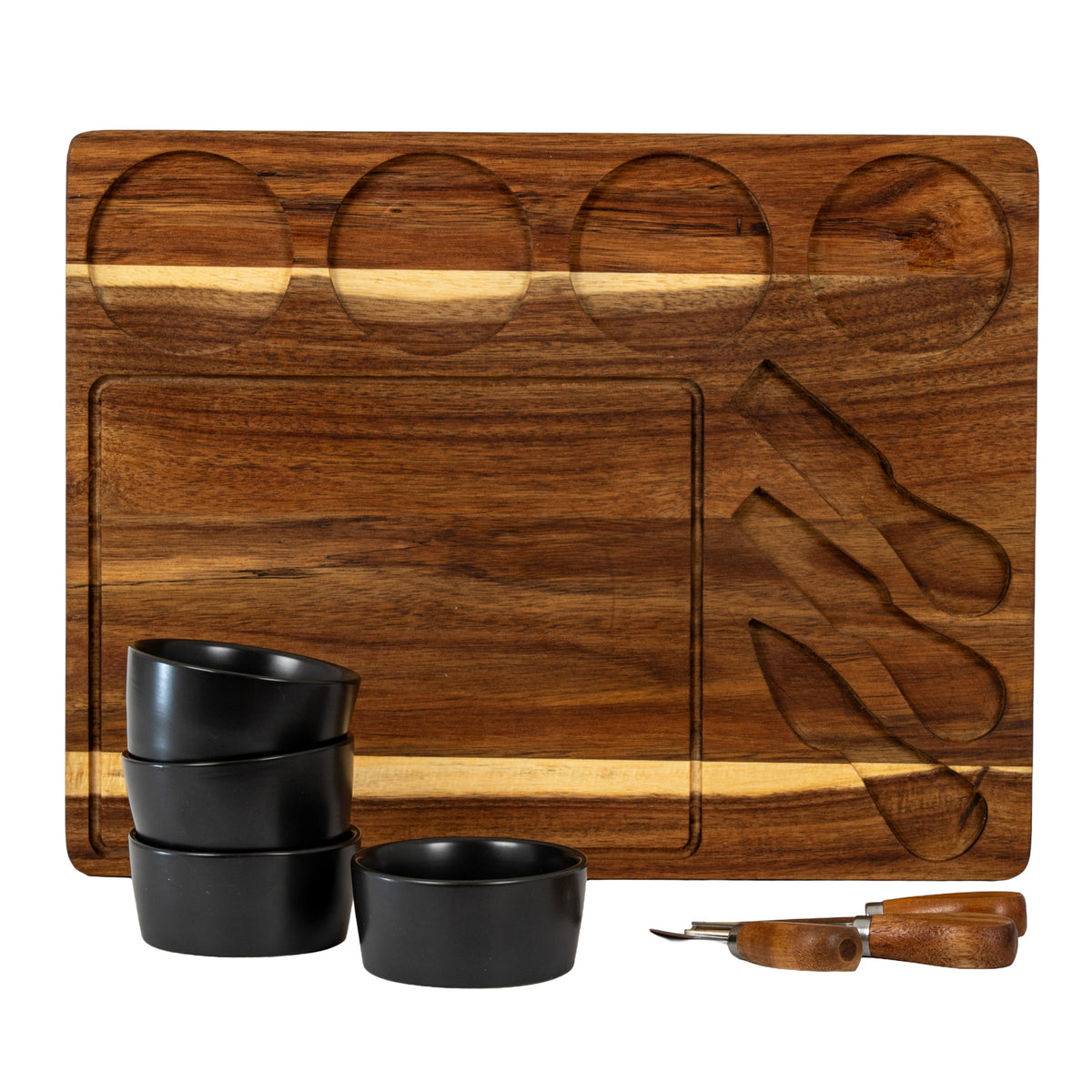 Cheese board displayed with its four circular recesses and three shaped utensil slots empty, with dark bowls and rounded-handle utensils arranged in front.