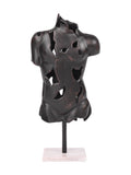 Dark textured torso sculpture with irregular openings and warm highlights, raised on a black stem above a pale rectangular marble base.
