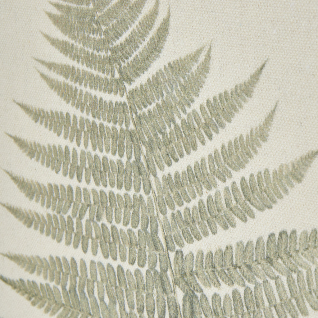 Close-up of the fern's finely divided green leaflets against the cream woven texture.