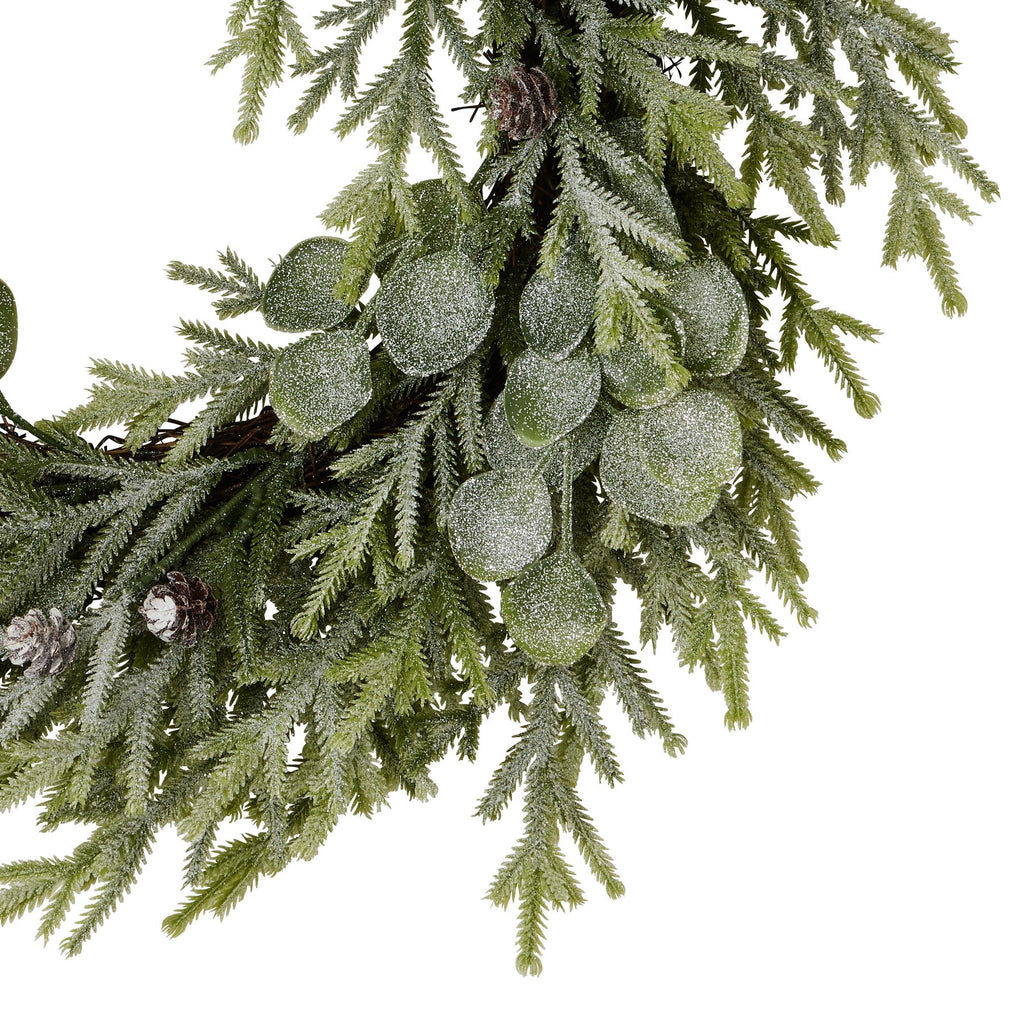 Close-up of frosted rounded leaves and fine green sprigs, with brown pinecones and part of the twig-like wreath ring visible.