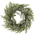 Front view of a circular green foliage wreath with white frosting, rounded leaves and small brown pinecones on a white background.