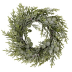 Front view of a circular green foliage wreath with white frosting, rounded leaves and small brown pinecones on a white background.