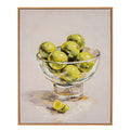 Front view of a portrait artwork in a slim warm-toned frame, showing yellow-green fruit in a clear-looking footed bowl and a cut wedge on a pale tabletop.