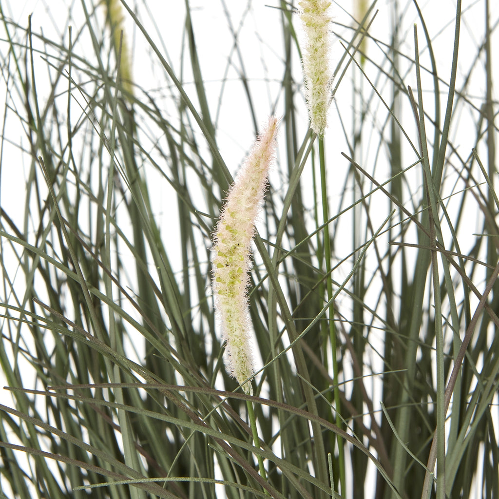 Close-up of pale fuzzy seed heads among crossing narrow green blades in the artificial grass arrangement.