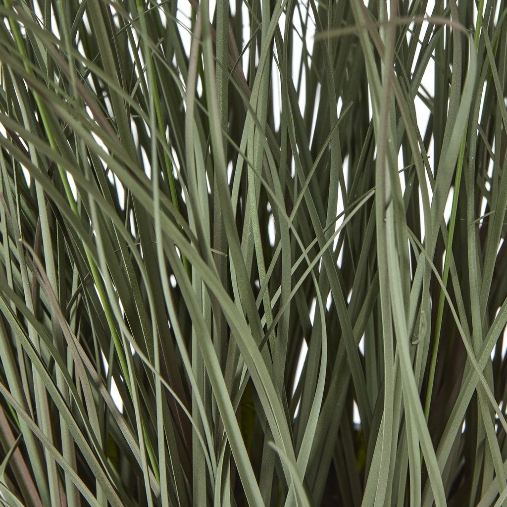Detail of densely overlapping muted green artificial grass blades, with thin stems crossing between them.
