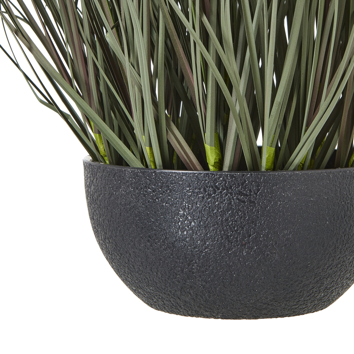 Close-up of the pebbled black bowl-shaped pot beneath the lower green blades of the artificial grass arrangement.