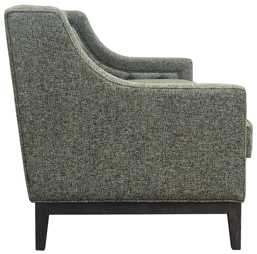 Side view showing the sofa’s curved arm, speckled green upholstery, piping and dark wooden rail with tapered legs.