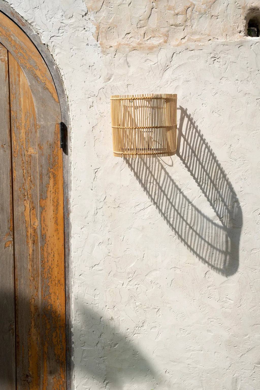 Gigi Rattan Wall Applique – Natural, Small – wall-mounted outdoors with a long geometric shadow