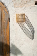 Gigi Rattan Wall Applique – Natural, Small – wall-mounted outdoors with a long geometric shadow