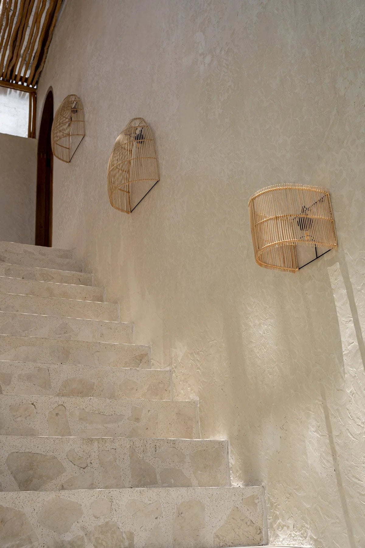 Gigi Rattan Wall Applique – Natural, Small – three wall lights arranged along a stairway