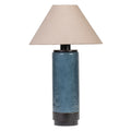 Dolphin-blue cylindrical table lamp with a glossy, subtly mottled body, dark base and upper trim, and a broad tapered natural fabric shade on white.