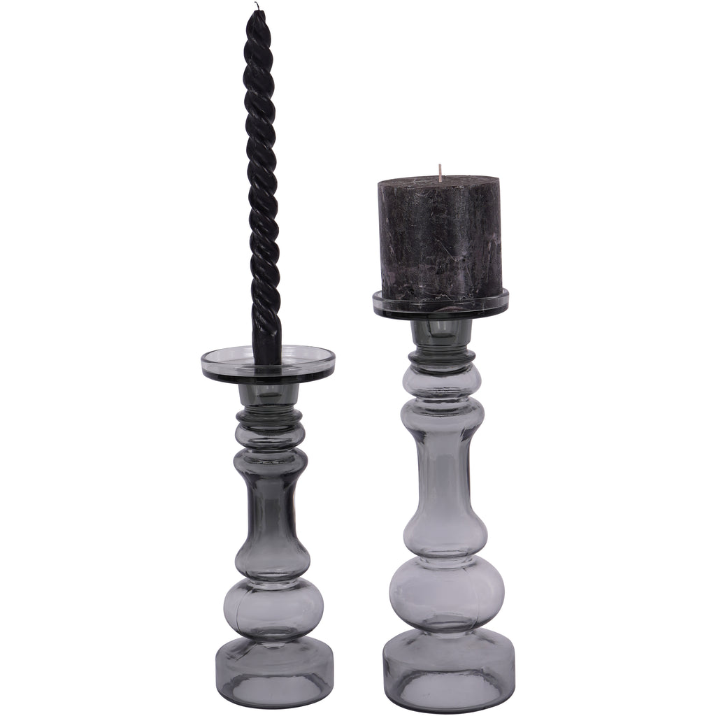 Two smoky grey glass candle holders, with a dark pillar candle on the larger holder at right and a twisted candle on the smaller holder at left.