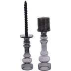 Two smoky grey glass candle holders, with a dark pillar candle on the larger holder at right and a twisted candle on the smaller holder at left.