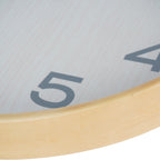 Low angled close-up of the clock's natural-toned frame and glass-covered face beside the numerals four and five.
