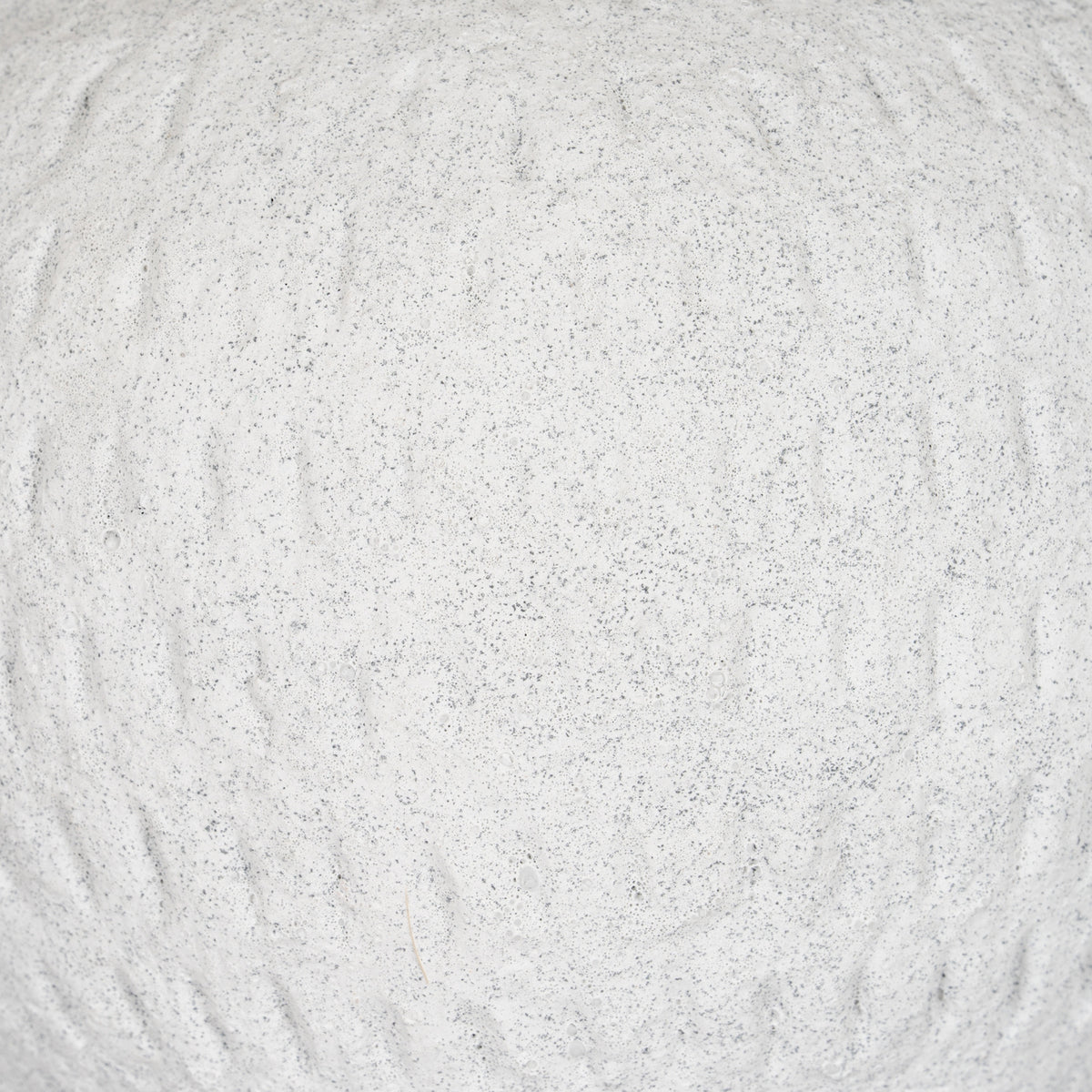Detail of the vase's pale granular surface, with fine grey speckles and irregular shallow vertical strokes.