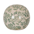 Cream decorative ball covered in green flowers and leaves, showing fine crackle lines and bright surface reflections against a white background.