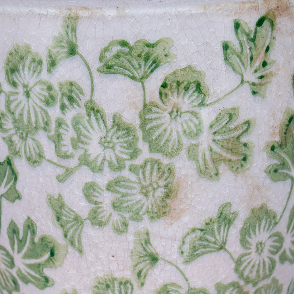 Detail of pale green flowers and curling leaves with darker green accents, fine crackling and tan marks on a cream-white background.