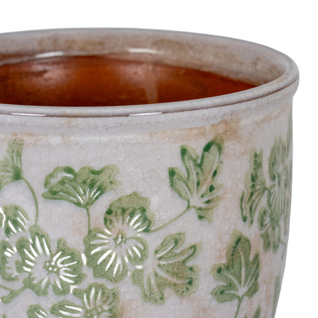 Close view of the planter's rounded rim and brown interior above green flowers and leaves on the glossy crackled surface.