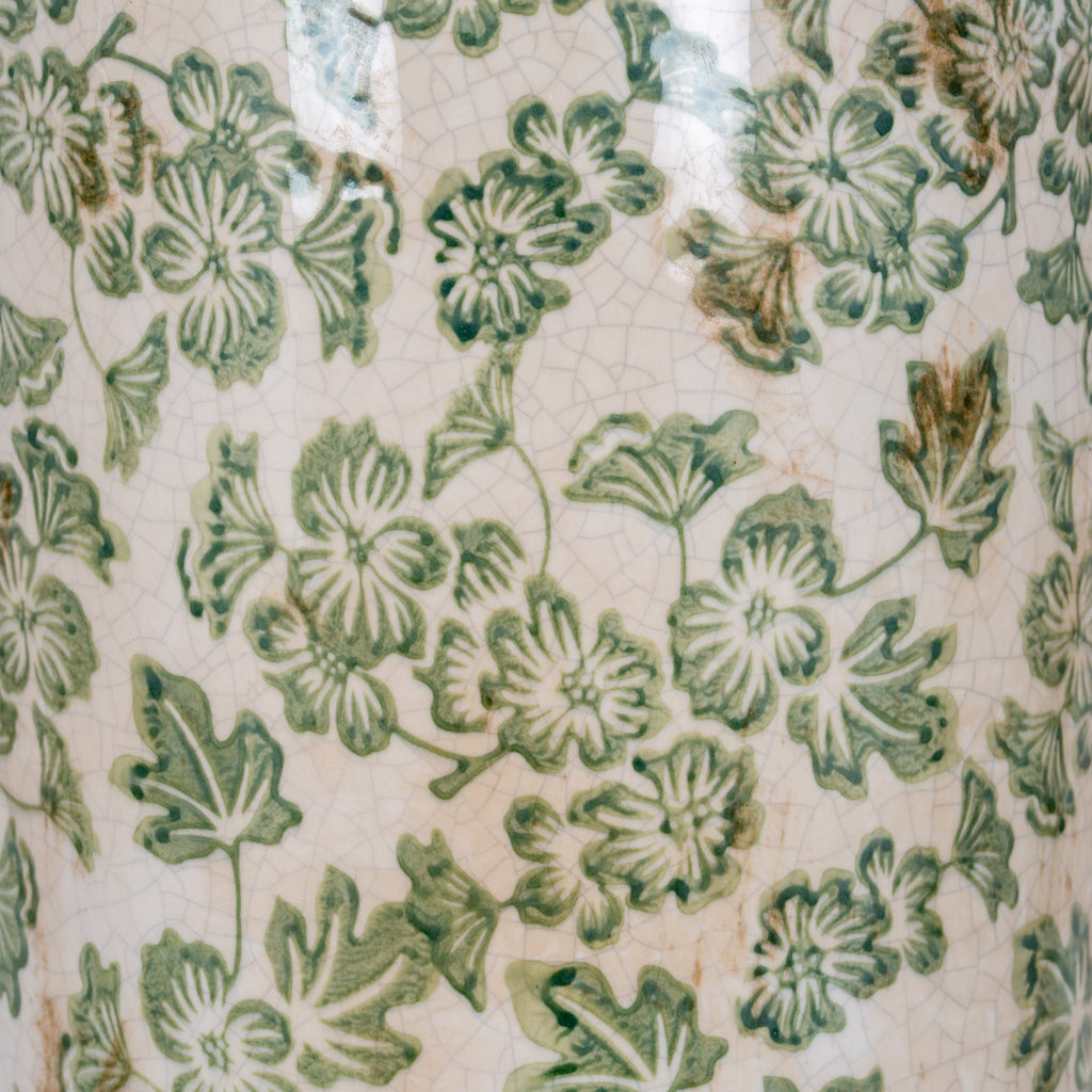 Detail of green flowers and leaves across the glossy cream-white vase surface, with fine crackle lines and scattered tan marks.