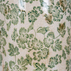 Detail of green flowers and leaves across the glossy cream-white vase surface, with fine crackle lines and scattered tan marks.