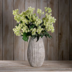 Styled arrangement of pale green meadow flower sprays in a tall textured grey vase on a wooden surface against vertical wood panelling.