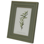 Angled view of the green-grey photo frame showing its stepped profile and right edge, with gold-tone lines and a botanical insert marked 4 x 6 inches.