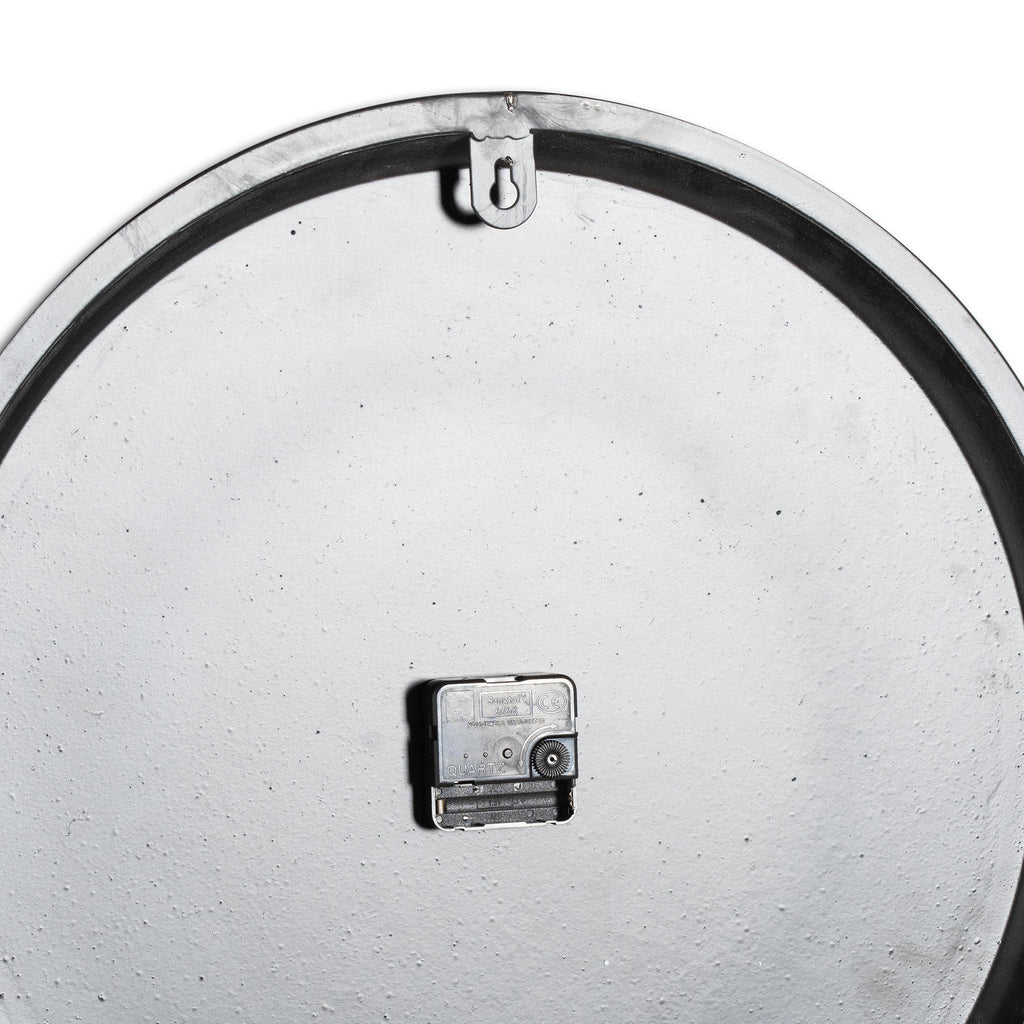 Rear view of the wall clock showing its pale textured back, black clock movement and keyhole-shaped hanging tab beneath the upper rim.
