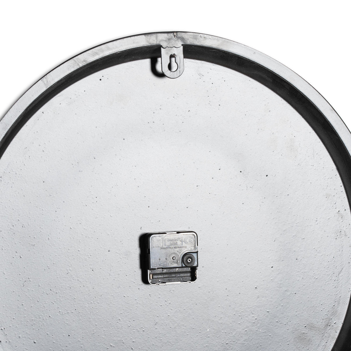 Rear view of the wall clock showing its pale textured back, black clock movement and keyhole-shaped hanging tab beneath the upper rim.