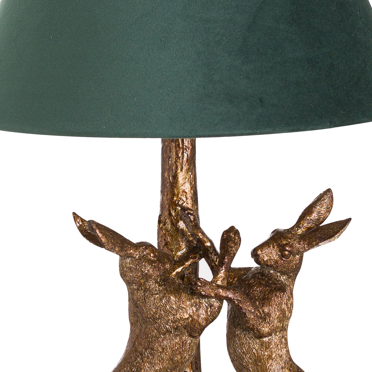 Close-up of the lamp's textured hare faces, long ears and raised forepaws beneath the green shade.
