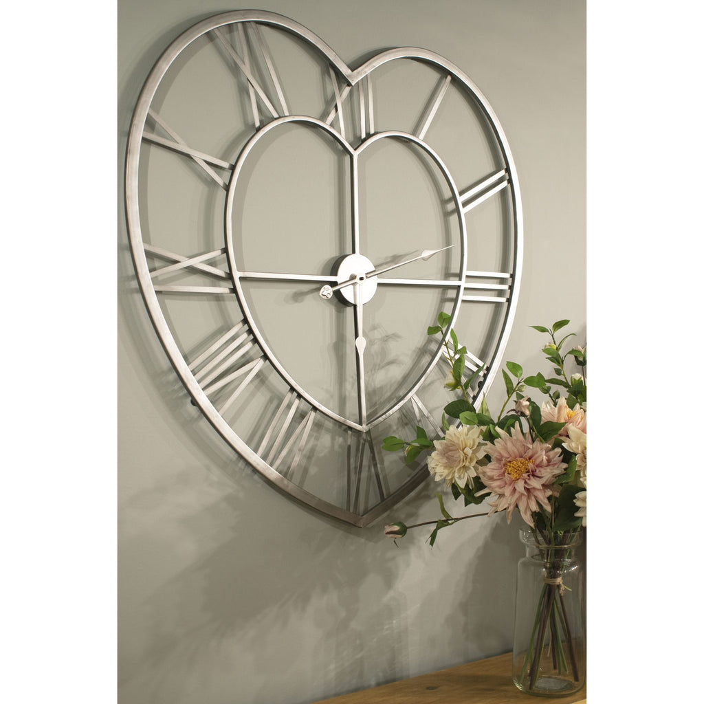 Heartframe Wall Clock on a muted green wall above a wooden surface, beside pale flowers in a clear glass vase.