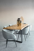 Herringbone dining table surrounded by grey upholstered chairs, styled with two ceramic vases and dried stems.