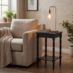 Holder Frame Table Lamp with a glowing bulb on a dark side table beside a cream armchair, styled with books and a mug in a neutral room.