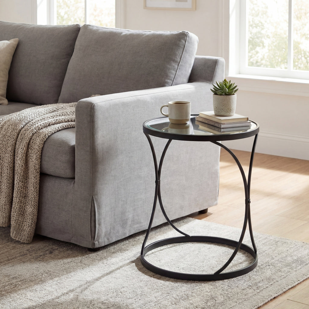 Mirrored round side table beside a grey sofa, styled with a mug, stacked books and a potted succulent on a pale rug.