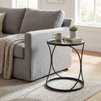 Mirrored round side table beside a grey sofa, styled with a mug, stacked books and a potted succulent on a pale rug.