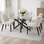 Clear-topped Intersecting Barbase Dining Table styled with pale upholstered chairs and white roses on a light rug in a panelled dining room.