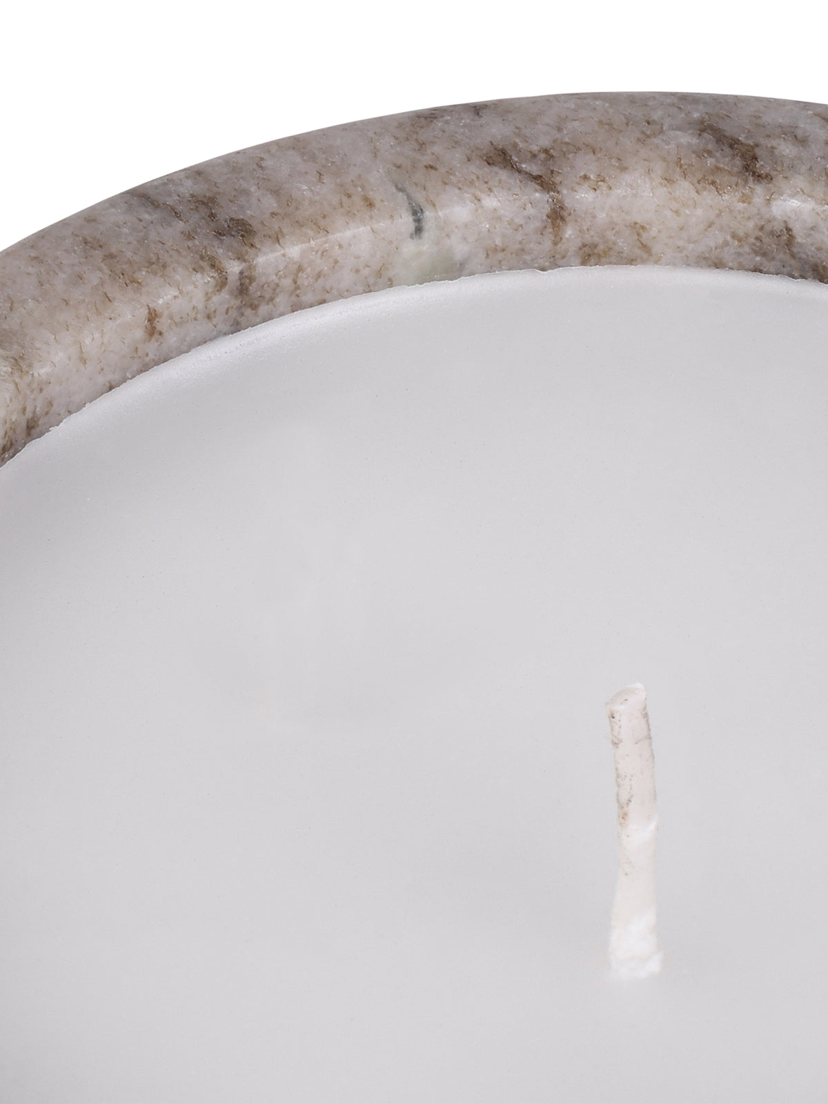 Close-up of the candle's white wax and unlit wick beside the beige marble rim with brown and grey mineral markings.