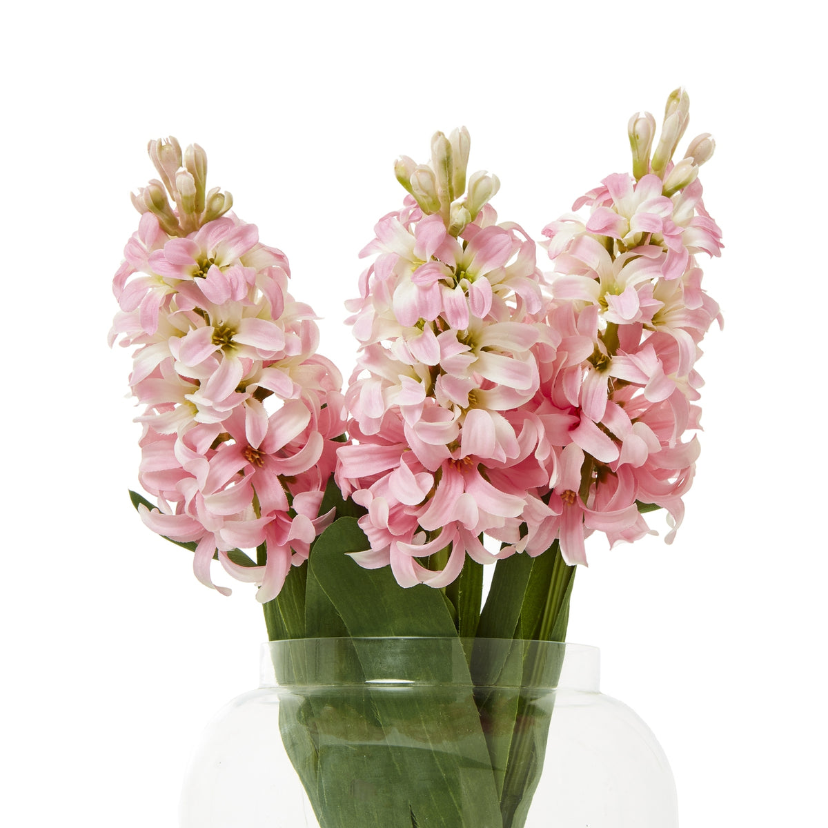 Three pink artificial flower spikes with pale buds and broad green leaves arranged in a clear rounded vase against white.