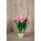 Three pink artificial flower stems arranged in a pale green bowl on a wooden surface against vertical wooden panelling.
